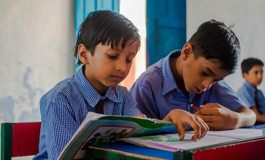 Two boys sharing a textbook at a school desk