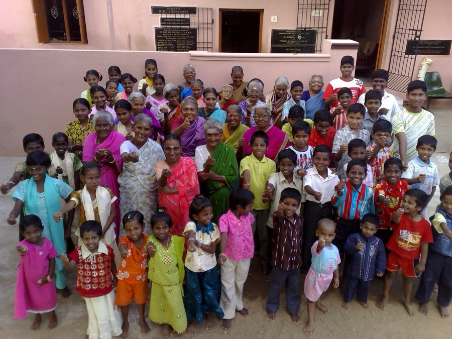 Children and elderly women gathered together in the courtyard of a community home in Tamil Nadu