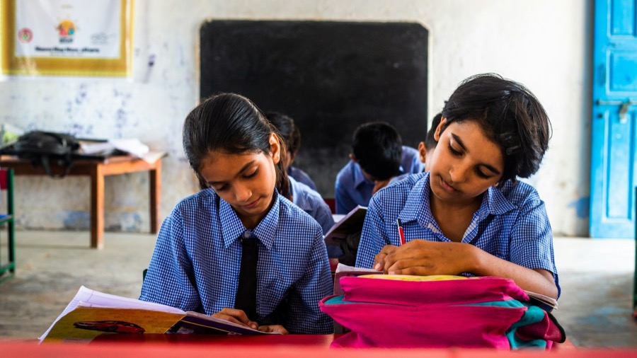 Two girls in school uniform writing at a classroom desk