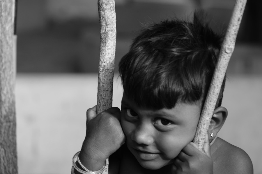 A young boy in Tamil Nadu smiling while holding a tree branch