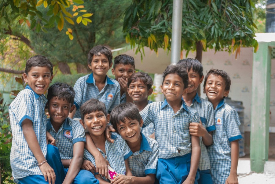 A group of boys in blue school uniforms smiling outside their village school
